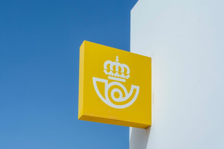 A yellow postal sign with a crown logo against a clear blue sky, representing mail services.